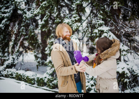 Junge kaukasier Junge mit Bart und ein Mädchen haben ein Datum im Freien im Winter Park vor dem Hintergrund eines schneebedeckten Nadelbaumbaum spielen Schneebälle, Thr Stockfoto