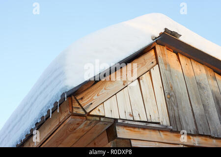 Dach der rustikalen hölzernen Gebäuden mit Schnee gegen den blauen Himmel in den Strahlen der untergehenden Sonne abgedeckt. Ansicht von unten Stockfoto