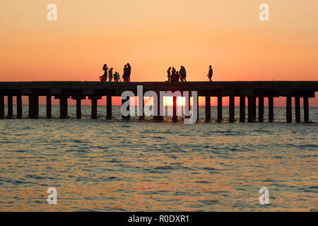 Gruppen von Menschen an der alten Pier genießen Sie den herrlichen Sonnenuntergang über der Küste des Schwarzen Meeres in der Republik Krim, Ukraine Stockfoto
