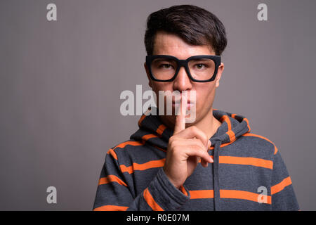 Jungen Asiatischen nerd Mann mit Kapuze gegen grauer Hintergrund Stockfoto