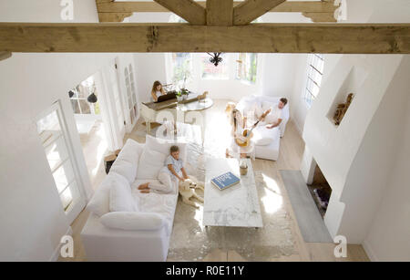 Hohe Betrachtungswinkel von Familie und Hund im Wohnzimmer, Tochter Klavier spielen, Mutter spielt Gitarre, Vater und Sohn auf den Sofas entspannen Stockfoto