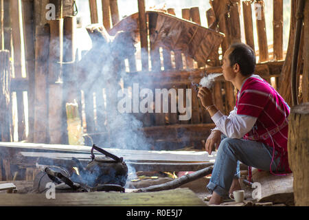 MAE KLANG Luang, Thailand, 2. Februar 2017: Karen Mann sitzt und raucht eine Zigarette, warten auf den Kaffee Wasser zum Kochen im Dorf o Stockfoto