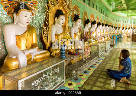 SAGAING, Myanmar, 20. JANUAR 2015: eine Frau sitzen auf dem Boden ist das beten Buddha vor einer langen Reihe von goldenen Statuen im U-Min Thonze pagod Stockfoto