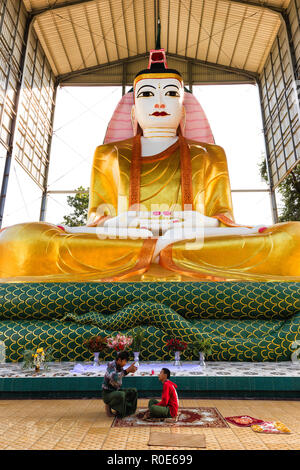 AMARAPURA, Myanmar, 20. JANUAR 2015: Zwei mens sitzen unter einem riesigen und bunten Buddha Statue in Amarapura Dorf in der Nähe von Mandalay, Myanmar (Bu Stockfoto