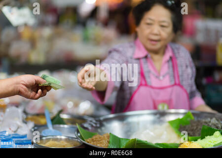 CHIANG MAI, Thailand, 30. Dezember 2014: Eine Frau wird mit einer Thai 20 Baht Banknote zu einem klebrigen Reis Verkäufer in der talat Pratu Markt in Chiang Mai, T Stockfoto
