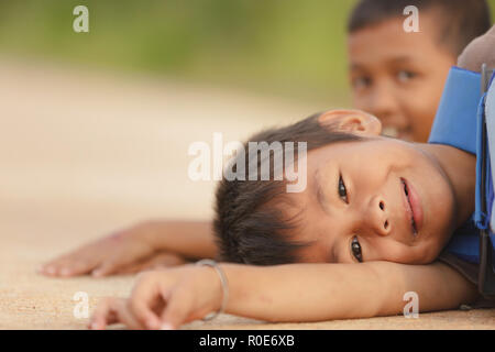 SATUN, Thailand, 09. Dezember 2011: Portrait Of Happy little boy liegen auf der Straße mit seinem Freund in einer sozialen Schule Waisenhaus in Satun, Thailand, Stockfoto