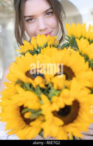 Junge Frau mit Sonnenblumen (Helianthus sp.). Stockfoto