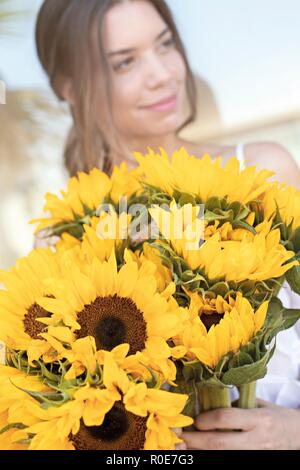 Junge Frau mit Sonnenblumen (Helianthus sp.). Stockfoto