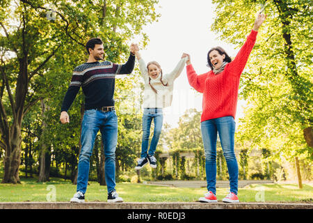 Lustige verspielte Kind Steine in den Händen der Eltern, die überglücklich. Vater und Mutter mit ihrer kleinen Tochter im Freien. Konzept der glücklichen Familie. Gleichheit Stockfoto