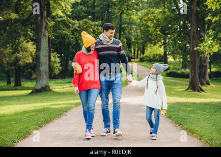 Paar schöne umfängt auch alle anderen, schaut auf ihre Kleinen gut aussehende Tochter, Spaziergänge über Green Park. Kleine niedliche Mädchen hält's Vater hat Stockfoto