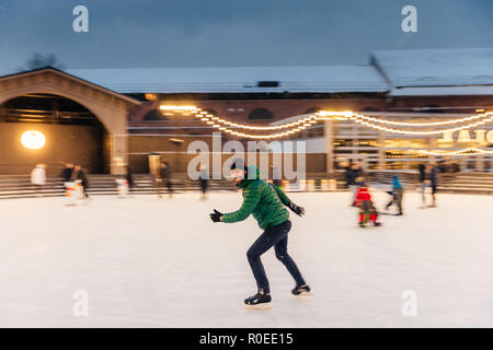 Fröhliche bärtiger Mann verbringt Weihnachten auf majestätische Eisbahn mit Lichtern geschmückt, Schlittschuhen auf dem Eis, hat Spaß, genießt sein Hobby und schneereiche Winter weath Stockfoto