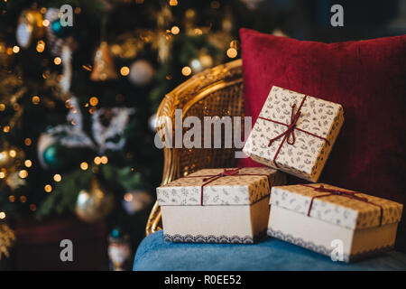 Bild von verpackten Geschenksets liegen auf Sessel gegen eingerichtet Neues Jahr Baum Hintergrund. Vorbereitung für den Urlaub. Schönen Weihnachtsbaum mit garla Stockfoto