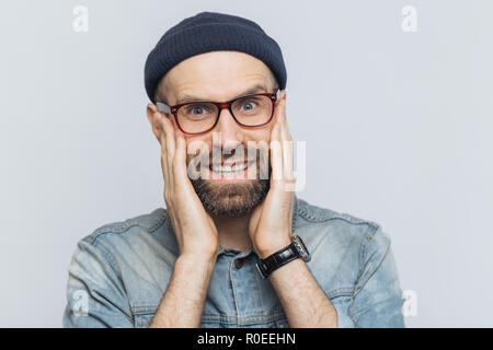 Portrait von attraktiven jungen Mann mit dicken Bart und Schnurrbart sieht mit Freude Ausdruck, hat weiße perfekte Zähne, posiert im Studio gegen leer Stockfoto