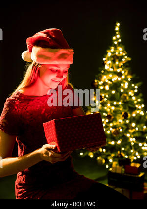 Junge Frau mit Geschenk, Weihnachtsbaum und dekorative Beleuchtung bokeh Hintergrund. Elf und mit Dekorationen aus Fichtenholz. Mädchen und schmücken. Stockfoto