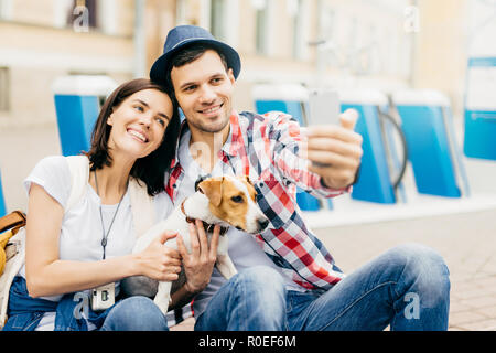 Portrait von fröhlichen Jungen gut aussehenden Frau an ihrem stattlichen Mann lehnt, freudig lächelnd in die Kamera, während posieren für selfie. Familie Mitglieder tr Stockfoto