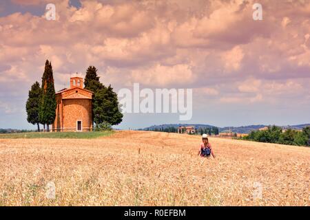Toskana, Italien - Juli 6, 2018: Cappella di Vitaleta, Val d'Orcia in der Toskana, Italien. Frau wandern in einem Feld von Roggen. Stockfoto