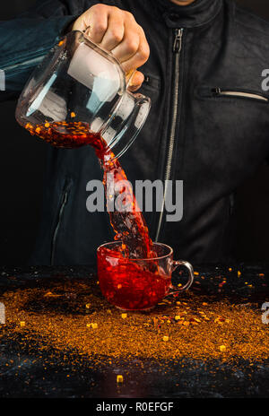 Ein Mann gießt ein Getränk aus einer Kanne in ein Glas Schale, können Sie sehen, Tropfen und Spritzwasser Stockfoto