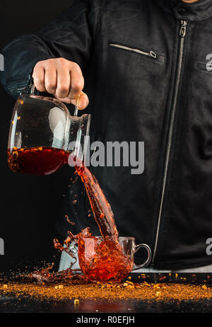 Ein Mann gießt ein Getränk aus einer Kanne in ein Glas Schale, können Sie sehen, Tropfen und Spritzwasser Stockfoto