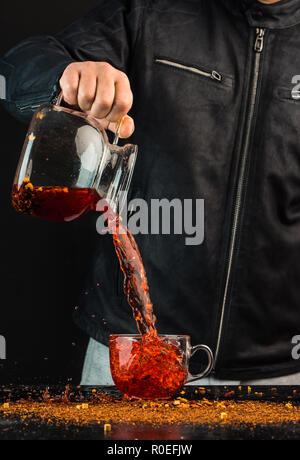 Ein Mann gießt ein Getränk aus einer Kanne in ein Glas Schale, können Sie sehen, Tropfen und Spritzwasser Stockfoto