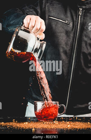 Ein Mann gießt ein Getränk aus einer Kanne in ein Glas Schale, können Sie sehen, Tropfen und Spritzwasser Stockfoto