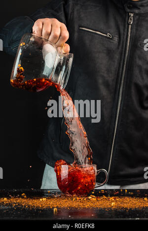 Ein Mann gießt ein Getränk aus einer Kanne in ein Glas Schale, können Sie sehen, Tropfen und Spritzwasser Stockfoto