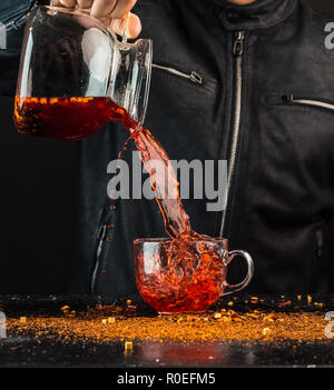 Ein Mann gießt ein Getränk aus einer Kanne in ein Glas Schale, können Sie sehen, Tropfen und Spritzwasser Stockfoto