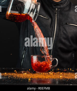 Ein Mann gießt ein Getränk aus einer Kanne in ein Glas Schale, können Sie sehen, Tropfen und Spritzwasser Stockfoto