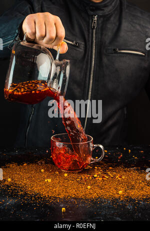 Ein Mann gießt ein Getränk aus einer Kanne in ein Glas Schale, können Sie sehen, Tropfen und Spritzwasser Stockfoto