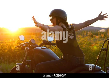 Eine Frau reiten Ihr Harley Davidson in den Sonnenuntergang und das Gefühl glücklich die Freiheit der einen Road Trip zu fühlen. Stockfoto