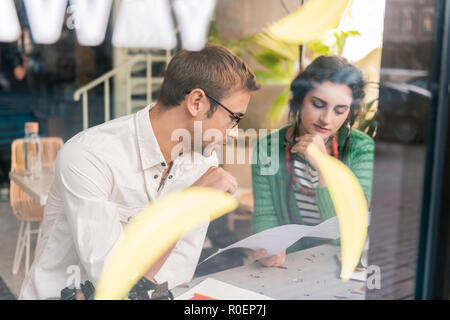 Dunkelhaarige mann Brille im Menü in der Nähe von Frau sitzen auf der Suche Stockfoto