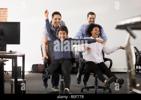 Glücklich, multi-ethnischen Büro Menschen Spaß reiten auf Stühlen Stockfoto