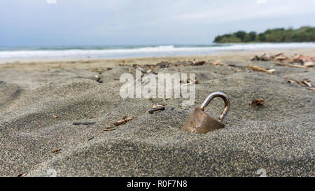 Goldene Vorhängeschloss auf einem dunklen Sandstrand Stockfoto