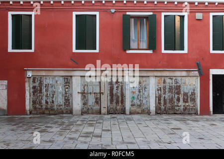 Ein rotes Haus mit grünen Fensterläden in einer leeren gepflasterten Straße in Venedig, Italien Stockfoto