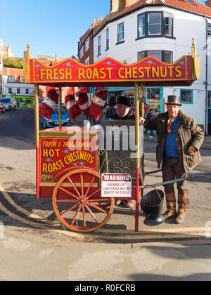 Heiße Kastanien Anbieter in traditioneller Kleidung verkaufen Nüsse geröstet auf ihre Hand Warenkorb in Whitby, North Yorkshire Stockfoto