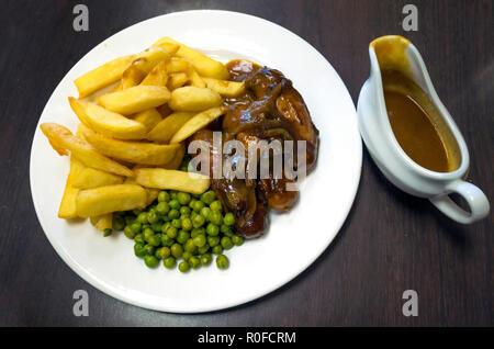 Lecker Mittag essen Yorkshire Wurst und Zwiebeln Kartoffelscheiben, Erbsen und eine kleine Kanne Senf Sauce Stockfoto