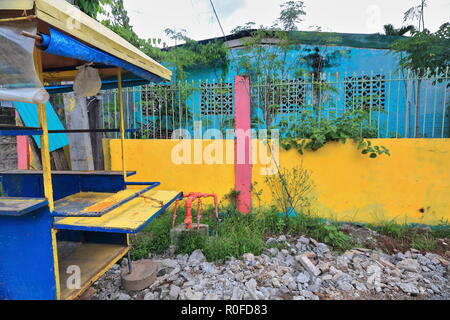 Abgebrochene foodcart lackiert Gelb und Blau neben dem gelben Betonwand eines blauen Haus mit Gitter Zaun auf der Seite einer Straße im Cen Stockfoto