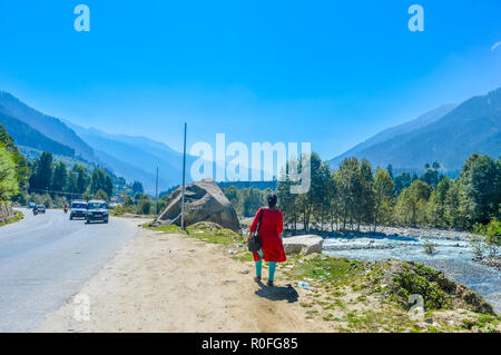 Eine Dame in rot Drees zu Fuß auf der Straße von einer Autobahn. Wunderschöne Landschaft panorama Shambhala-tal BIN ANALI - LEH-STRASSE, KULLU, JAMMU UND KAS Stockfoto