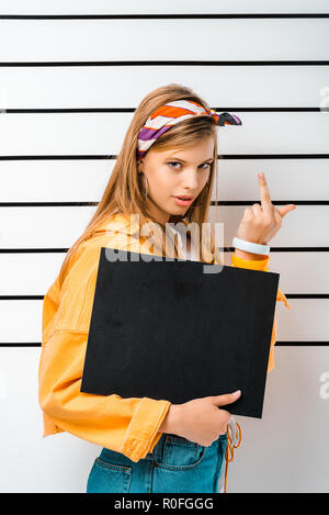 Hipster Mädchen mit leeren Gefängnis board Posing festgehalten und zeigt Mittelfinger vor Polizei Line up Stockfoto