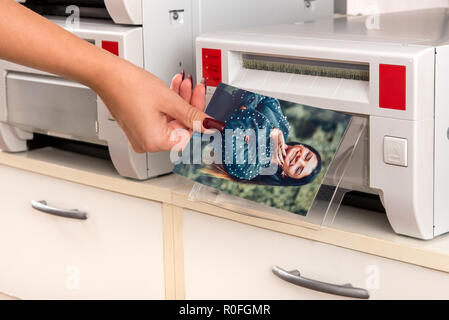 Frau mit einem farbigen Foto mit einem lächelnden hübsche Frau, die von einem Drucker in der Nähe zu sehen, der Hand und der Maschine Stockfoto