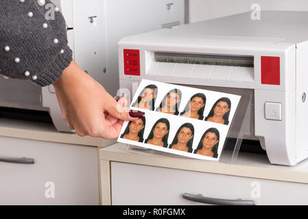 Der soeben gedruckten Passfotos, einer jungen Frau aus dem Drucker mit der Hand einer Frau, die für das Blatt in der Nähe zu sehen. Stockfoto