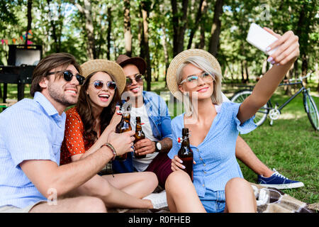 Lächelnd multikulturellen Freunde mit Bier unter selfie auf dem Smartphone während im Sommer Park ruhenden Stockfoto