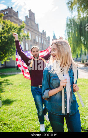 Selektiver Fokus der lächelnde Frau und Freund mit amerikanischen Fahne in der Hand im Park Stockfoto