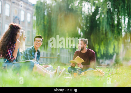 Lächelnd gemischtrassig Studenten in Park ruhenden mit Universität auf Hintergrund Stockfoto