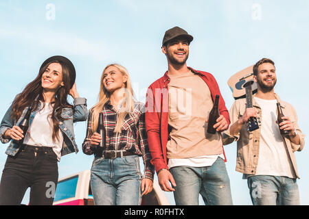 Ansicht von unten Gruppe der glückliche junge Menschen mit Bierflaschen und Gitarre zu Fuß durch Feld Stockfoto