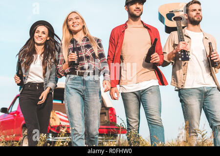 Ansicht von unten Gruppe junger Unholde mit Bierflaschen und Gitarre zu Fuß durch Feld Stockfoto