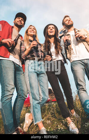 Ansicht von unten der Gruppe der jungen Menschen mit Bierflaschen und Gitarre auf Feld Stockfoto