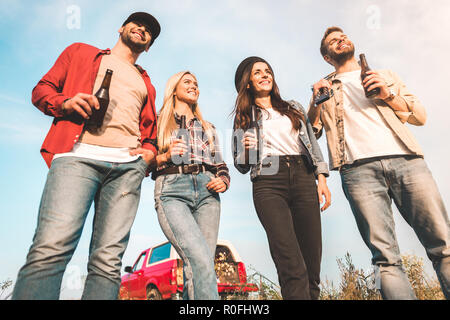 Ansicht von unten Gruppe der glückliche junge Menschen mit Bierflaschen und Gitarre auf Feld Stockfoto