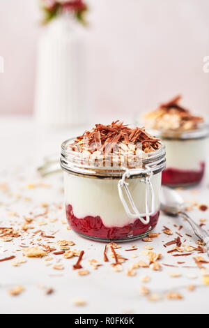 Gesundes Frühstück. Zwei Gläser der gesunden Joghurt mit Erdbeersauce, Hafer und Schokolade auf weißem Marmortisch. Schließen oben mit kopieren. Stockfoto