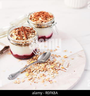 Gesundes Frühstück. Zwei Gläser der gesunden Joghurt mit Erdbeersauce, Hafer und Schokolade auf weißem Marmor Platte serviert. Platz crop. Stockfoto