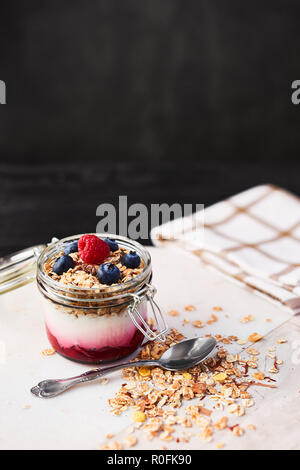 Gesundes Frühstück. Jar Gesunder Joghurt mit Himbeersauce, Hafer und Heidelbeeren auf weißem Marmor Servierteller über dunkle konkreten Hintergrund mit Co Stockfoto